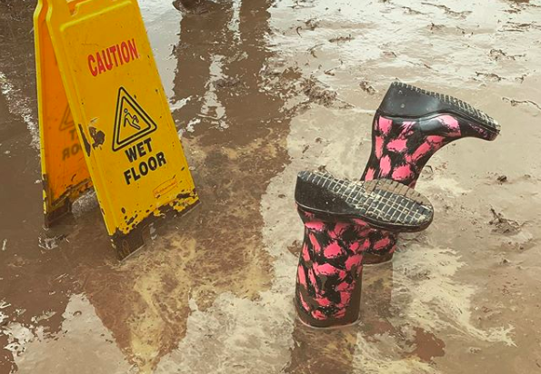 Wet floor sign on the very muddy ground at download festival with two wellies upside down in the mud