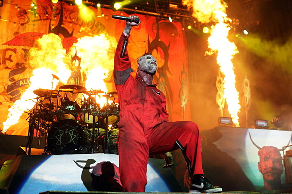 Corey Taylor in a red jumpsuit and mask in front of a lot of fire effects going off behind on on stage